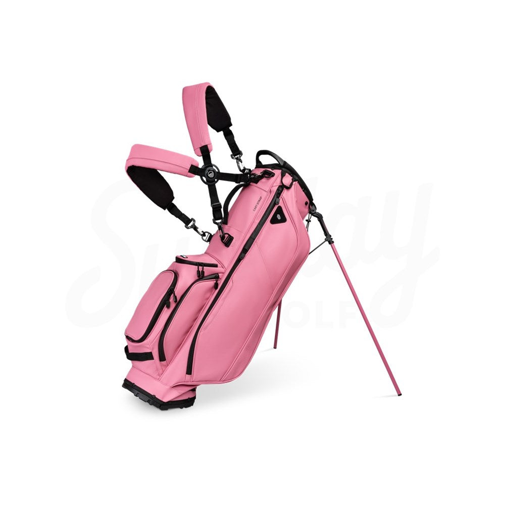 A dusty pink golf bag with black straps and details, equipped with multiple pockets, standing on a single golf cart approved stand.