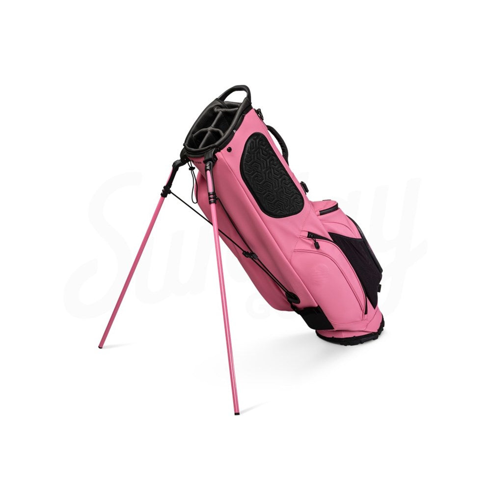 A dusty pink golf bag with black straps and details, equipped with multiple pockets, standing on a single golf cart approved stand.