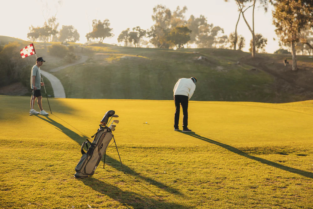 A gray Sunday Golf stand bag designed for golfers, featuring multiple pockets and a stand mechanism out in the field.