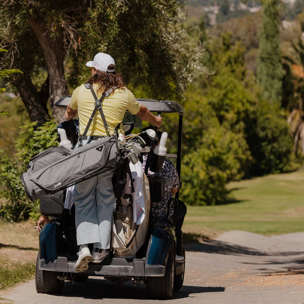 A full-size stand golf bag with multiple pockets, a built-in carry handle, and a backpack-style strap system with a golf cart out in the field.