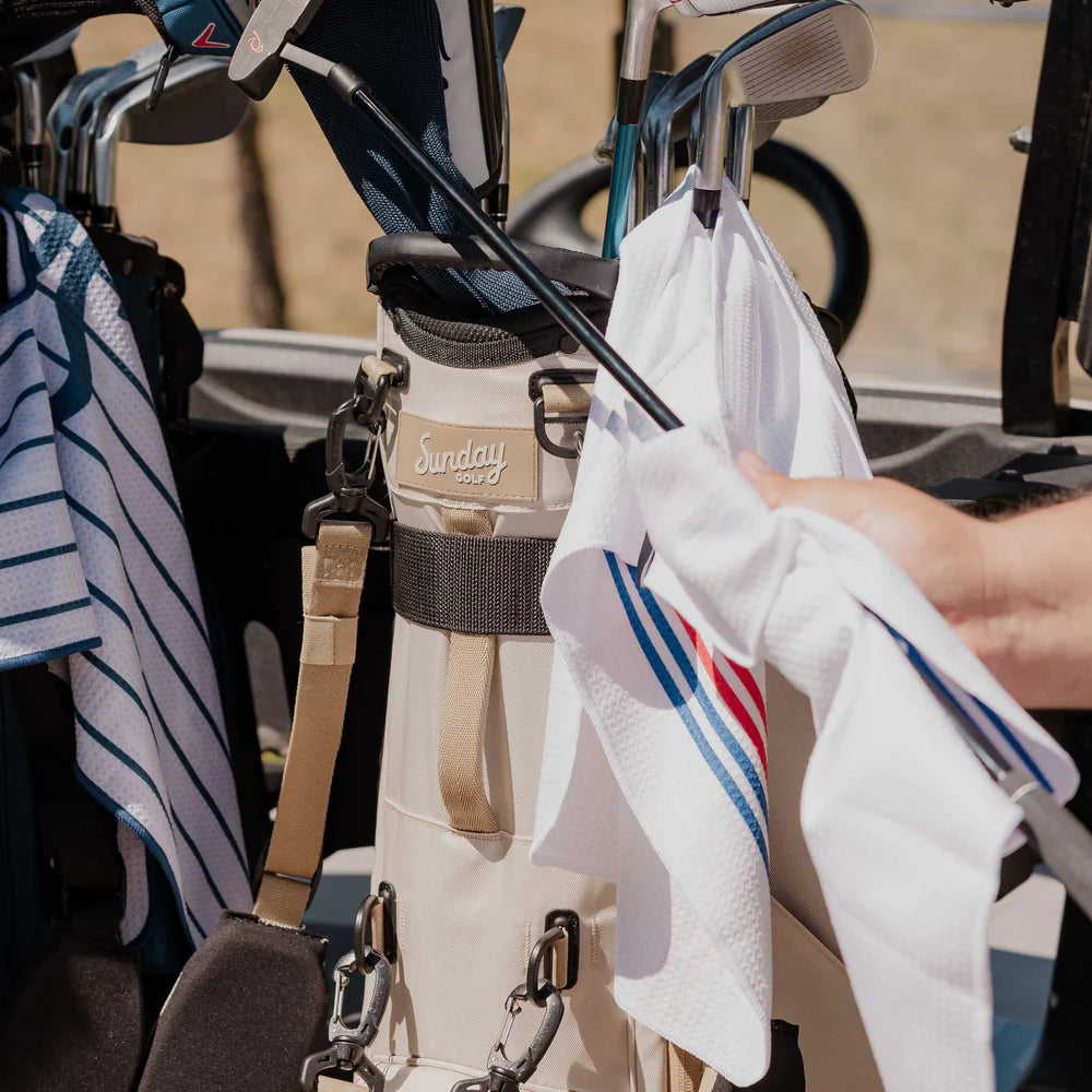 A full-size stand golf bag in beige and white, featuring multiple pockets, a built-in carry handle, and a backpack-style strap system being used.