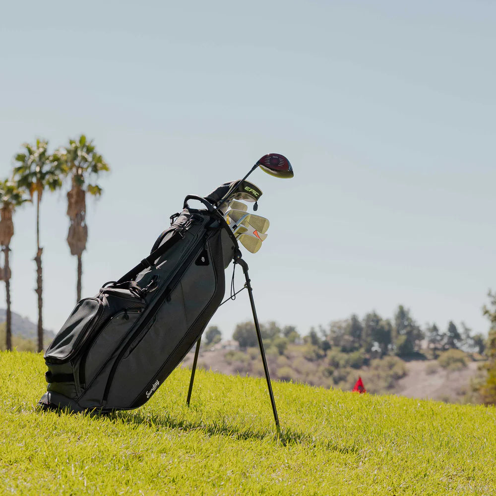 A full-size gray Sunday Golf stand bag with multiple pockets, a built-in carry handle, and a backpack-style strap system out in the field.