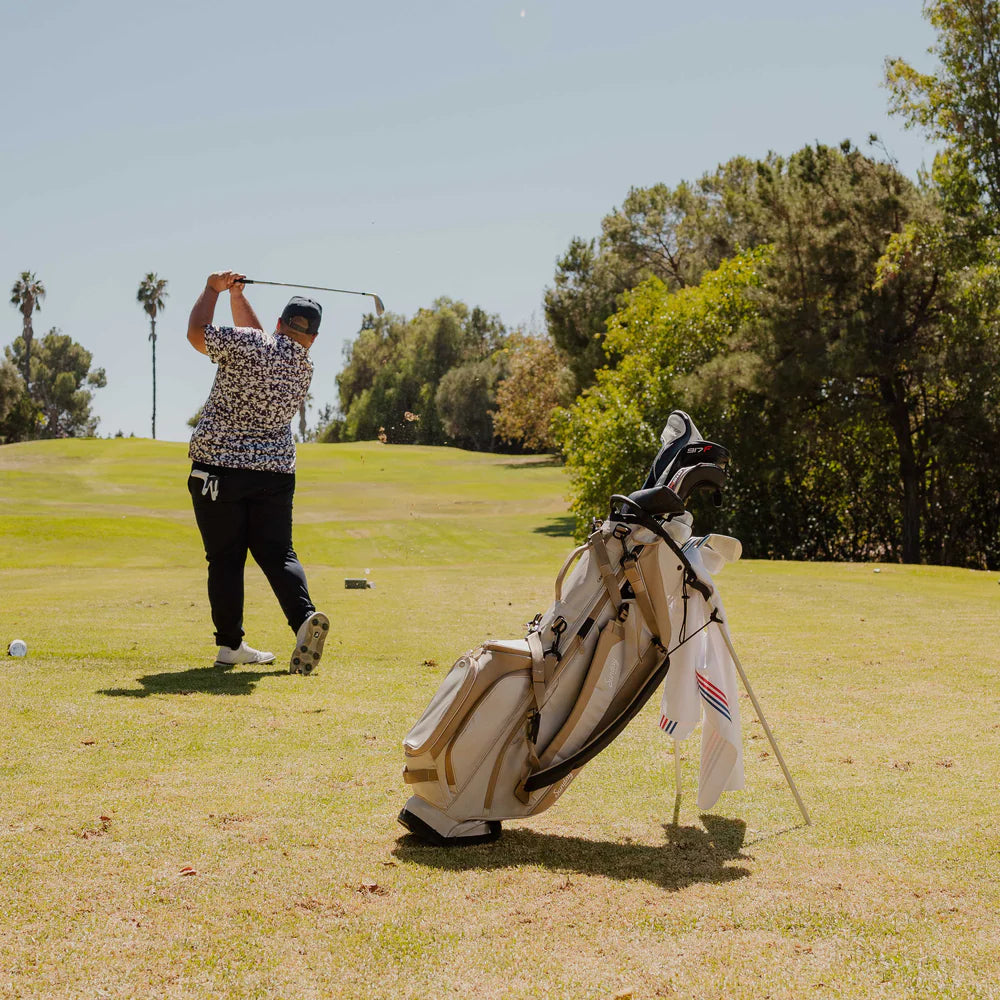 A full-size stand golf bag in beige and white, featuring multiple pockets, a built-in carry handle, and a backpack-style strap system with a model using the bag.