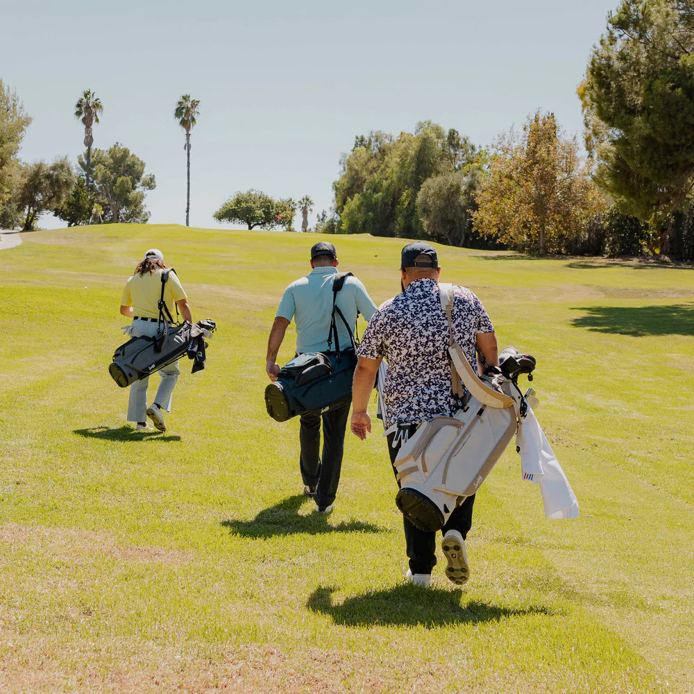 A full-size black golf stand bag with multiple pockets, a backpack-style strap, and a built-in carry handle, golfers out in the field.
