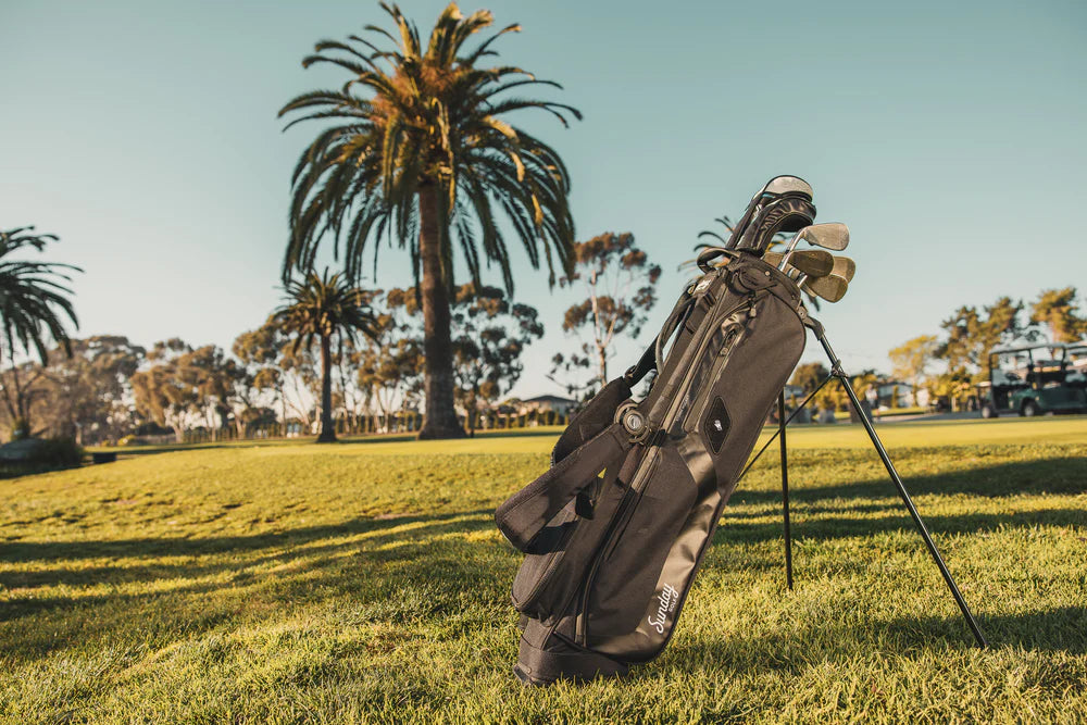 A black golf stand bag with multiple pockets and a dual-strap 4-way top divider, designed for holding up to 10 clubs. It is displayed out on the golf field